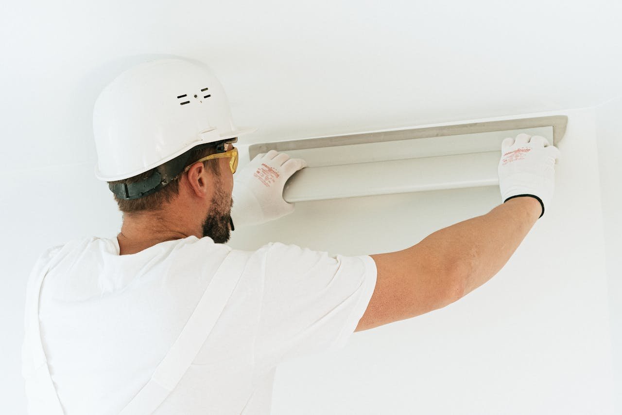 A construction worker wearing safety gear installs a light fixture in a modern indoor setting.